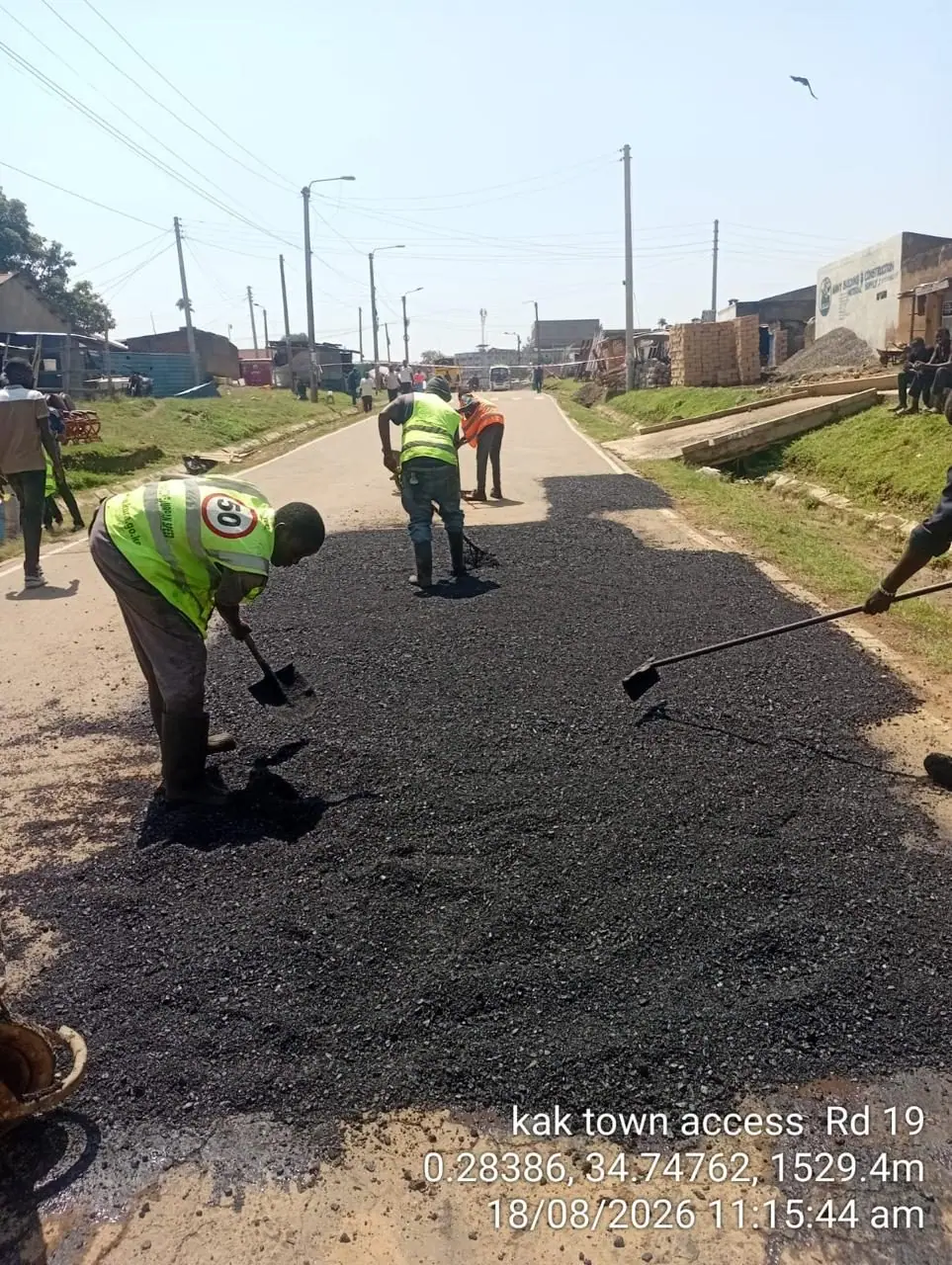 Three crew members raking and levelling hot asphalt across a carriageway in Kakamega town