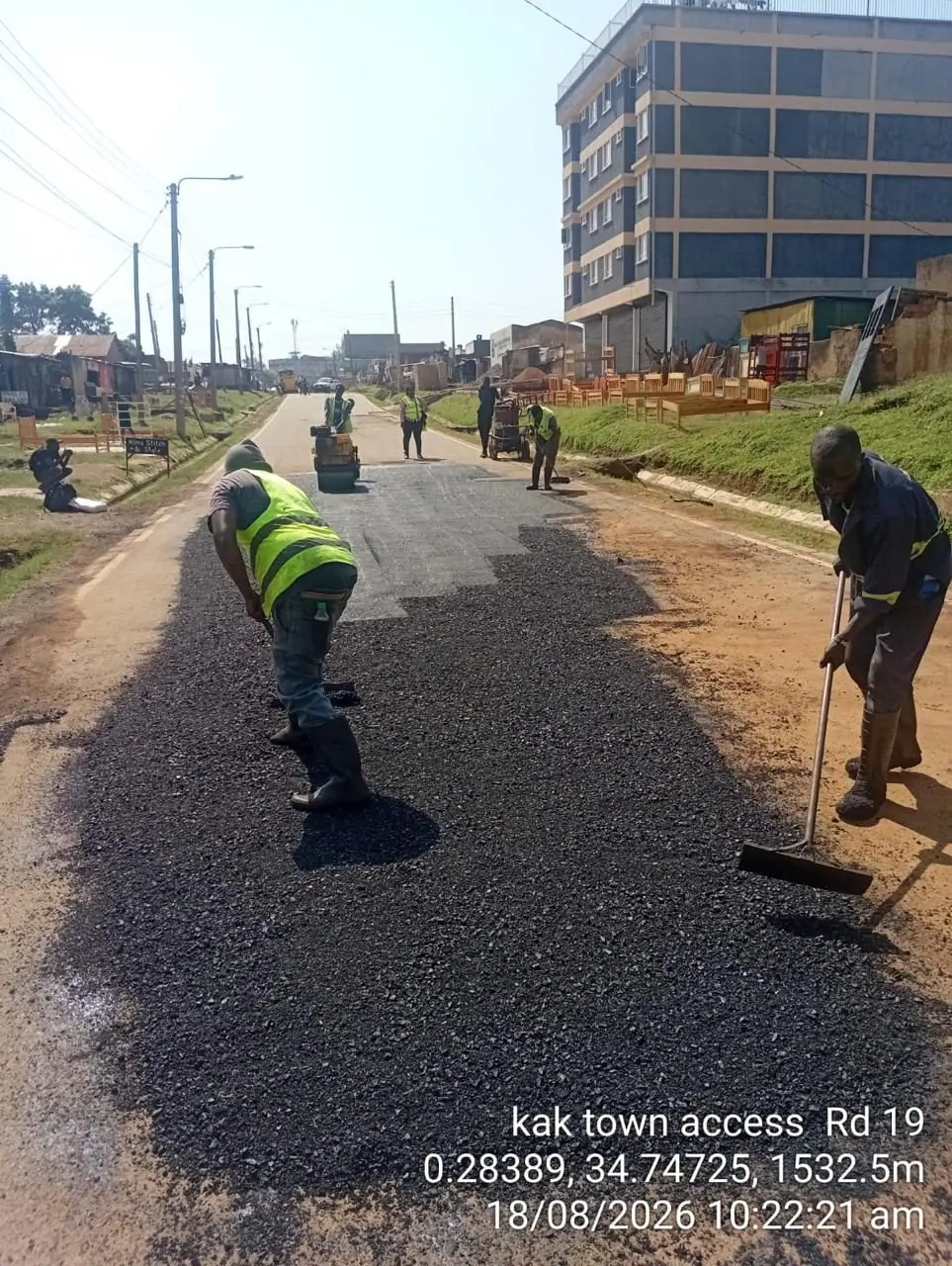 A crew member finishing the asphalt edge beside a freshly surfaced lane, with shopfronts behind