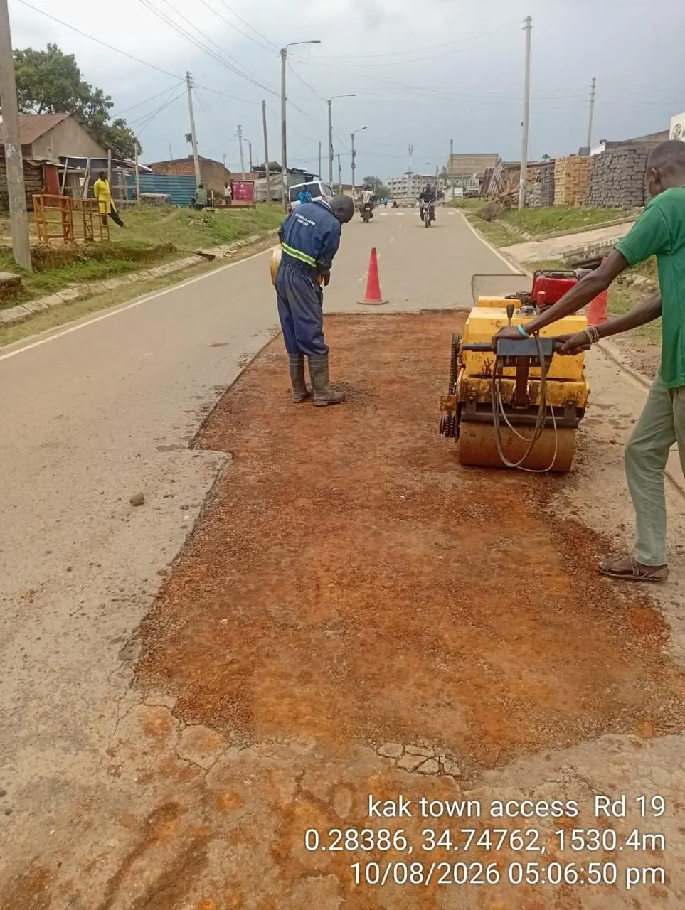 A pedestrian roller compacting a newly laid shoulder while a crew member guides it