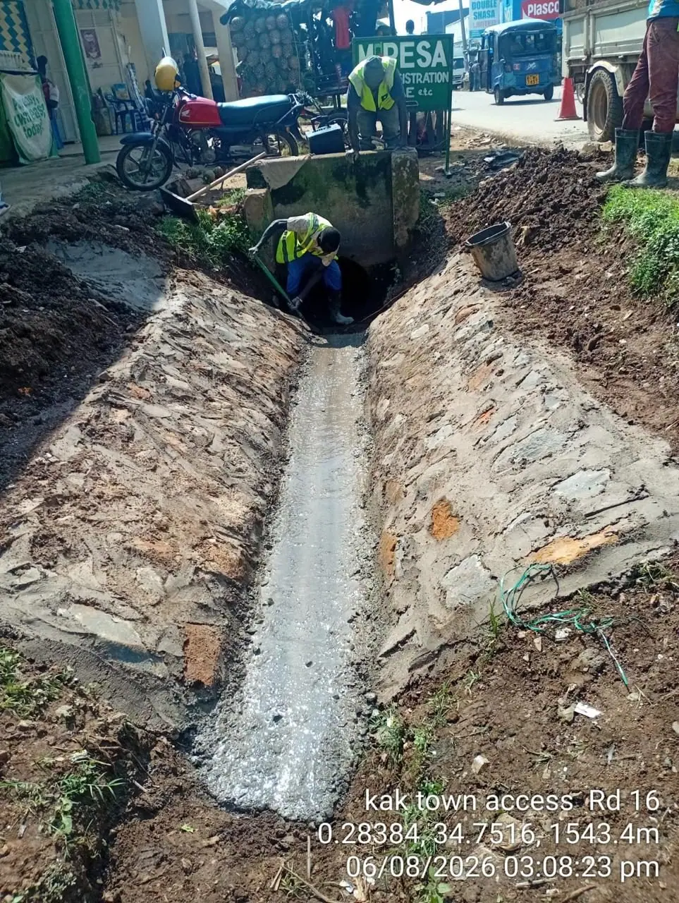 A completed stone-pitched drainage channel running alongside the road, a worker at the far end